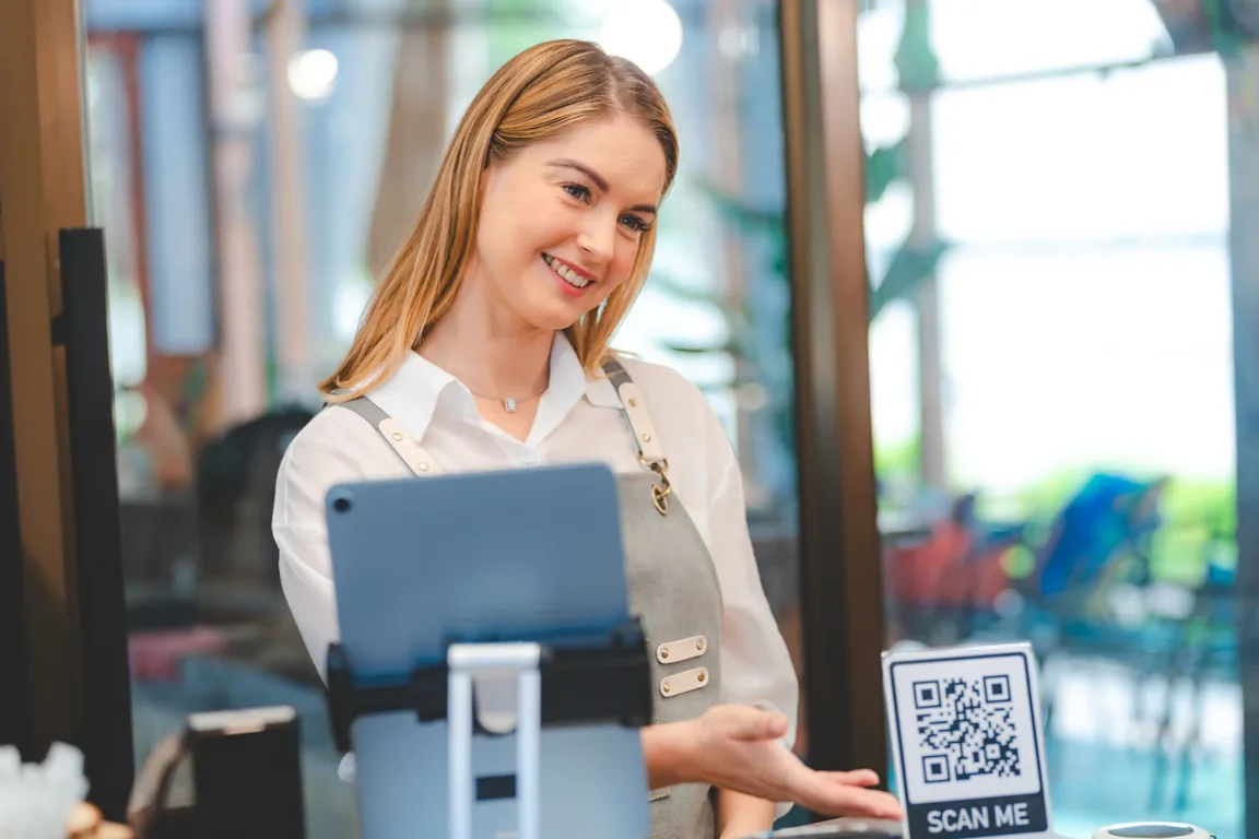 Mujer atendiendo una cafetería con un código QR sobre el mostrador